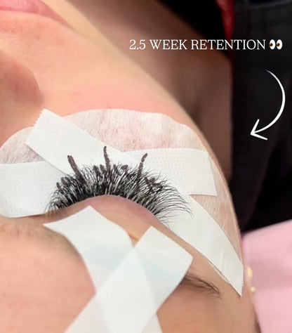 Eyelash extensions with adhesive tape on a person's eyelid, labeled '2.5 Week Retention'.
